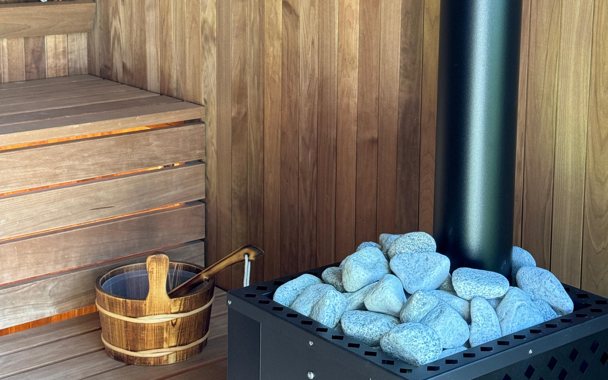 Outdoor sauna interior showing benches, heater and stones, bucket and ladle as visible condition context.