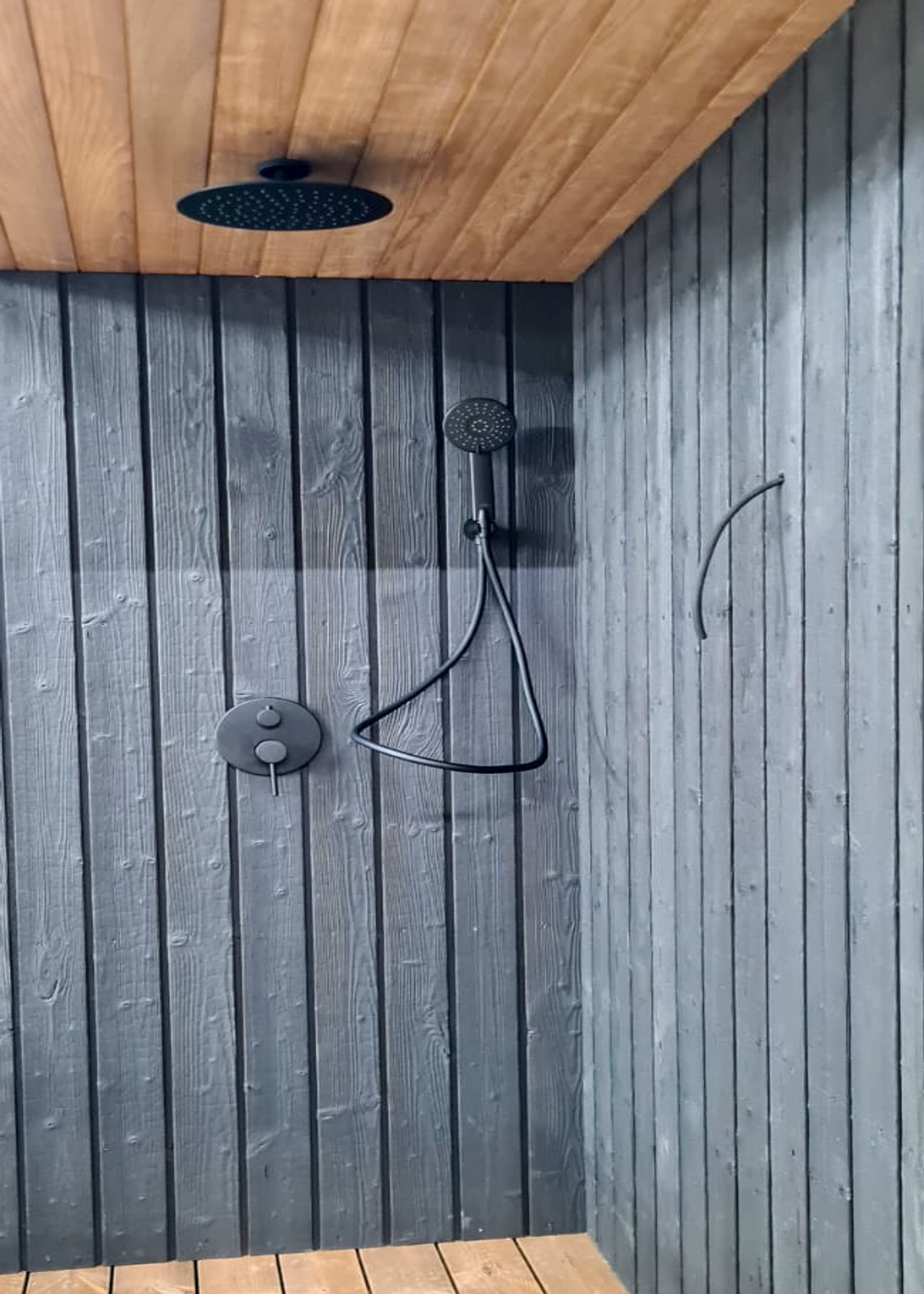 Real external overhead and hand-held rinse fixtures beside a sauna.