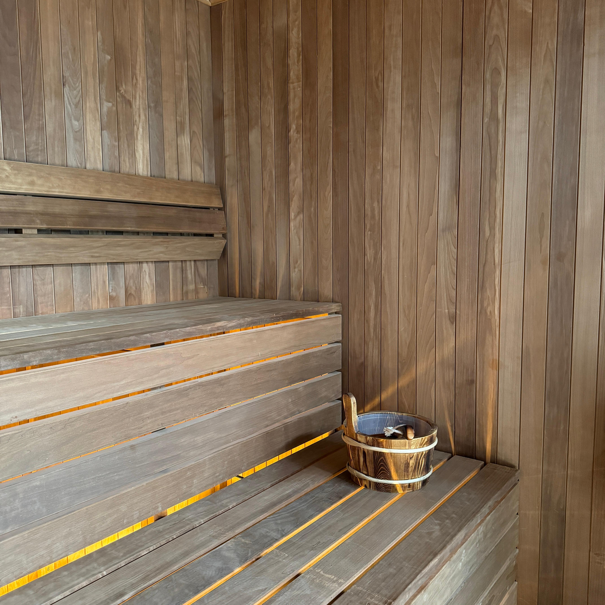 Real sauna interior with timber benches, bucket and ladle, used only as adjacent sauna context.